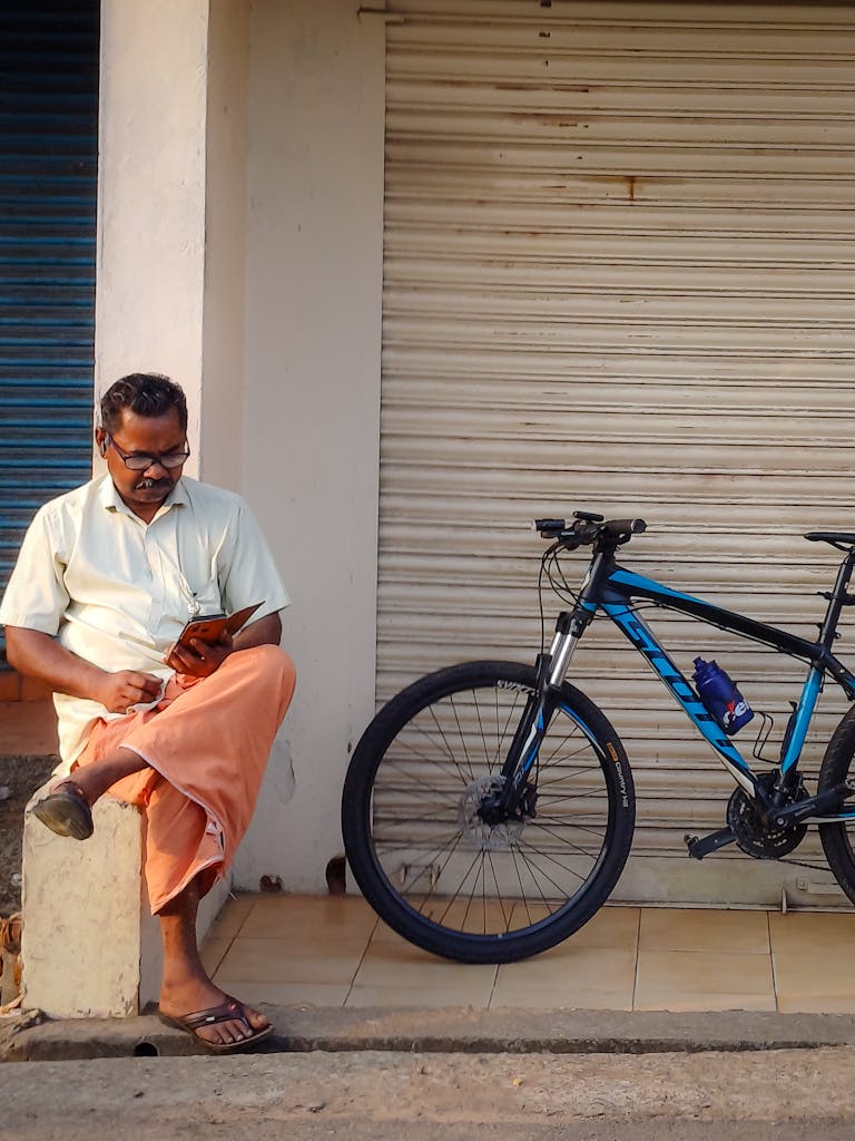 A man enjoys reading next to a bicycle in the streets of Kochi, India.